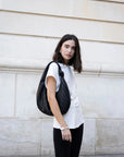 Femme portant une blouse blanche élégante col V minimaliste, avec un sac noir, dans un cadre urbain. Idéal pour un look chic et décontracté, mettant en avant la blouse blanche femme.