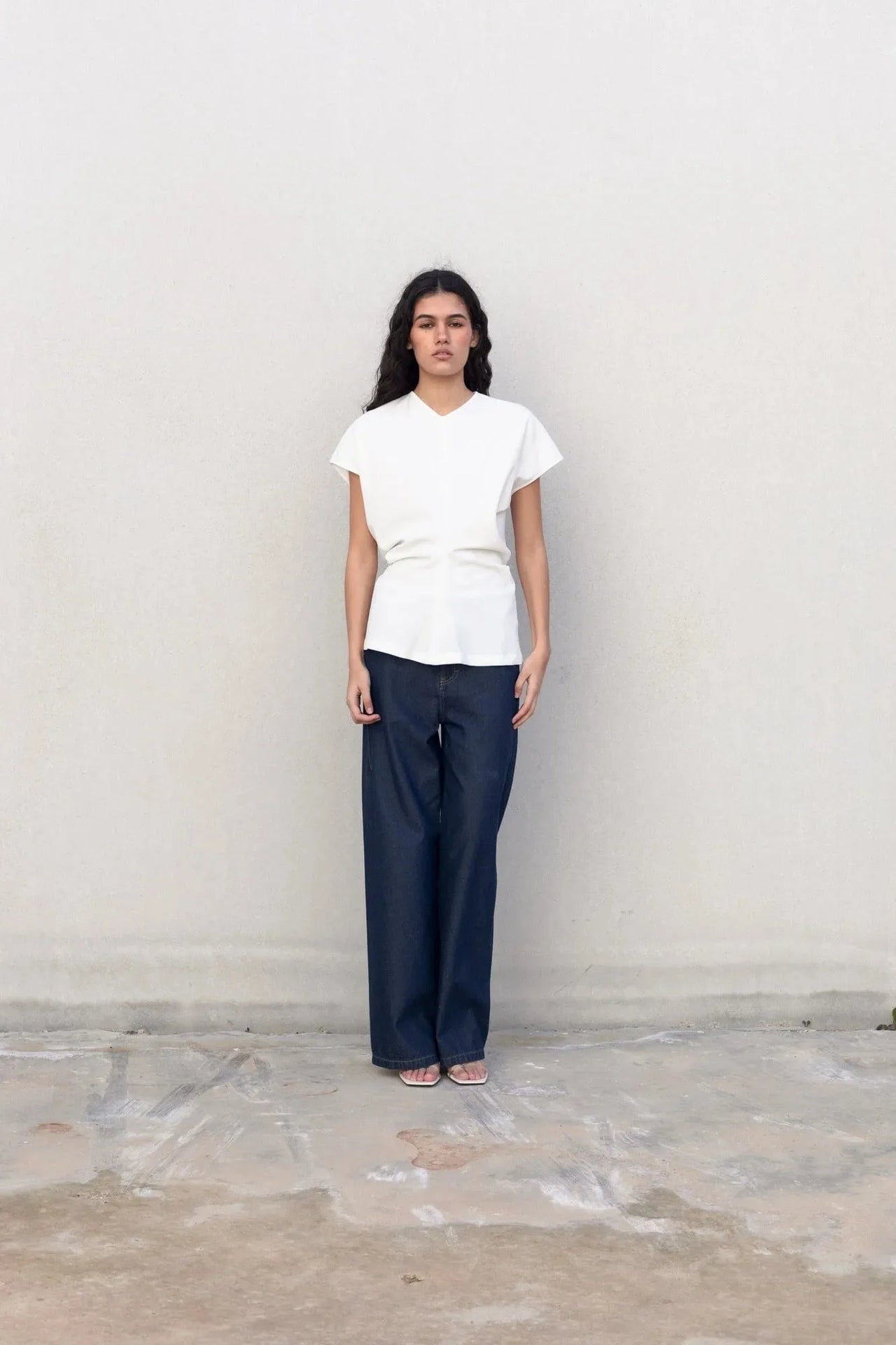 Modèle féminin portant une blouse blanche chic, avec un devant sur un fond neutre. La blouse blanche femme complète parfaitement un look modern.