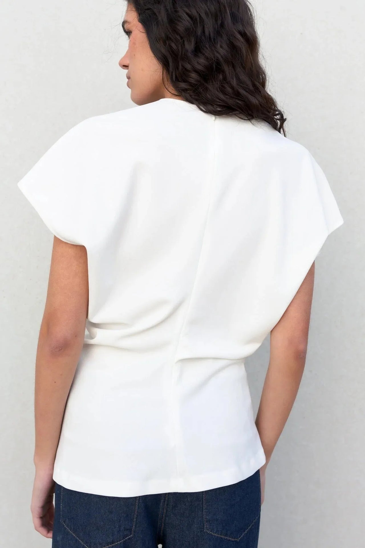 Image d'une femme de dos en blouse blanche minimaliste, prête à se démarquer avec élégance. La blouse blanche femme apporte une note chic à votre garde-robe.