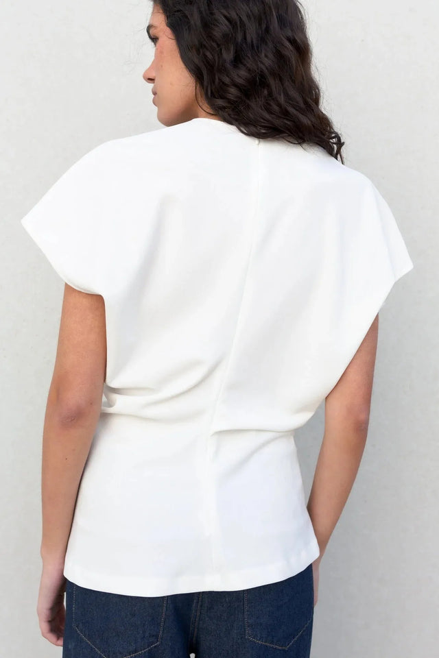 Image d'une femme de dos en blouse blanche minimaliste, prête à se démarquer avec élégance. La blouse blanche femme apporte une note chic à votre garde-robe.