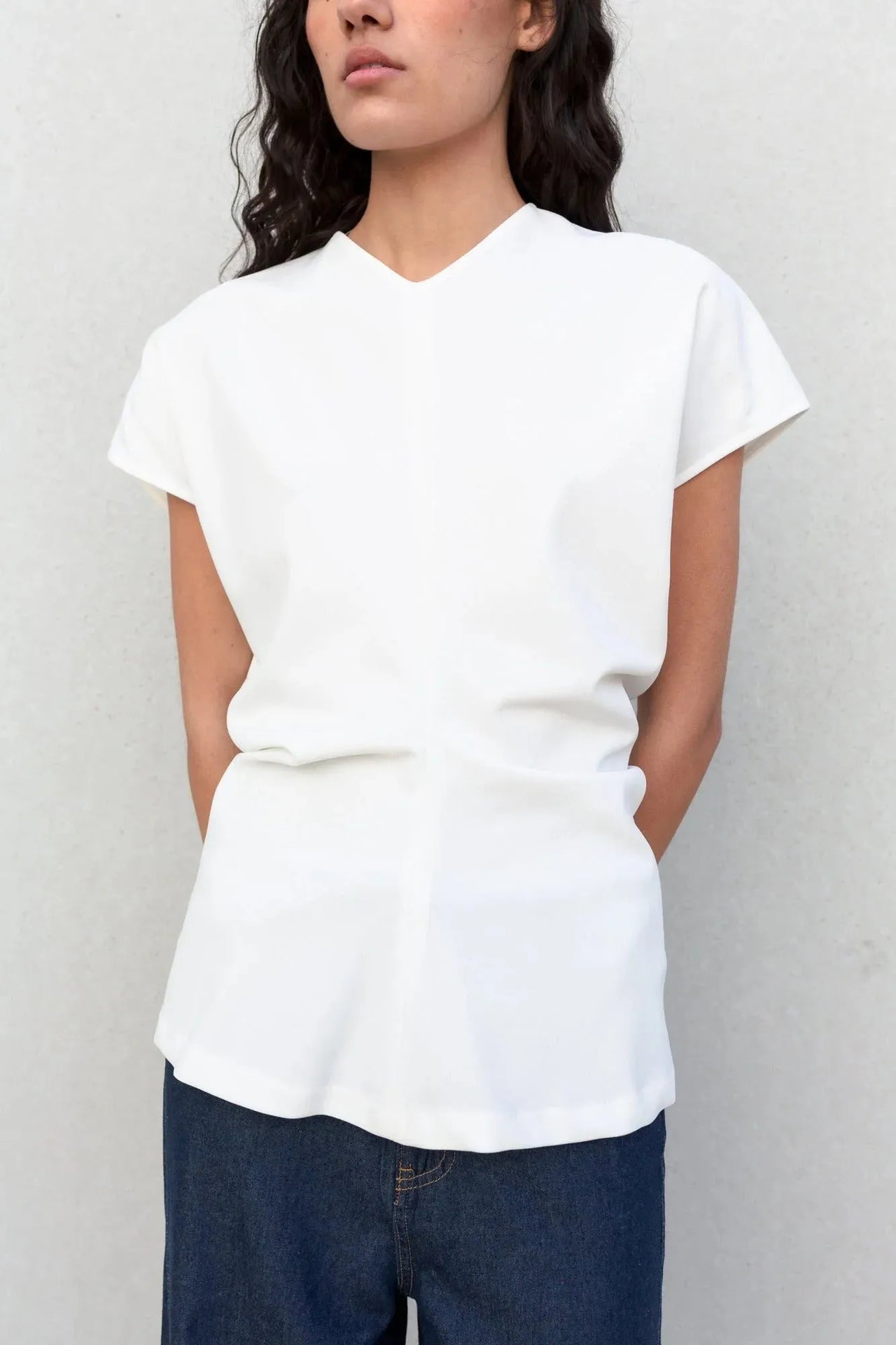 Vue rapprochée d'une femme en blouse blanche col V, stylée avec un look décontracté. Un choix parfait pour une blouse blanche femme élégante et confortable.
