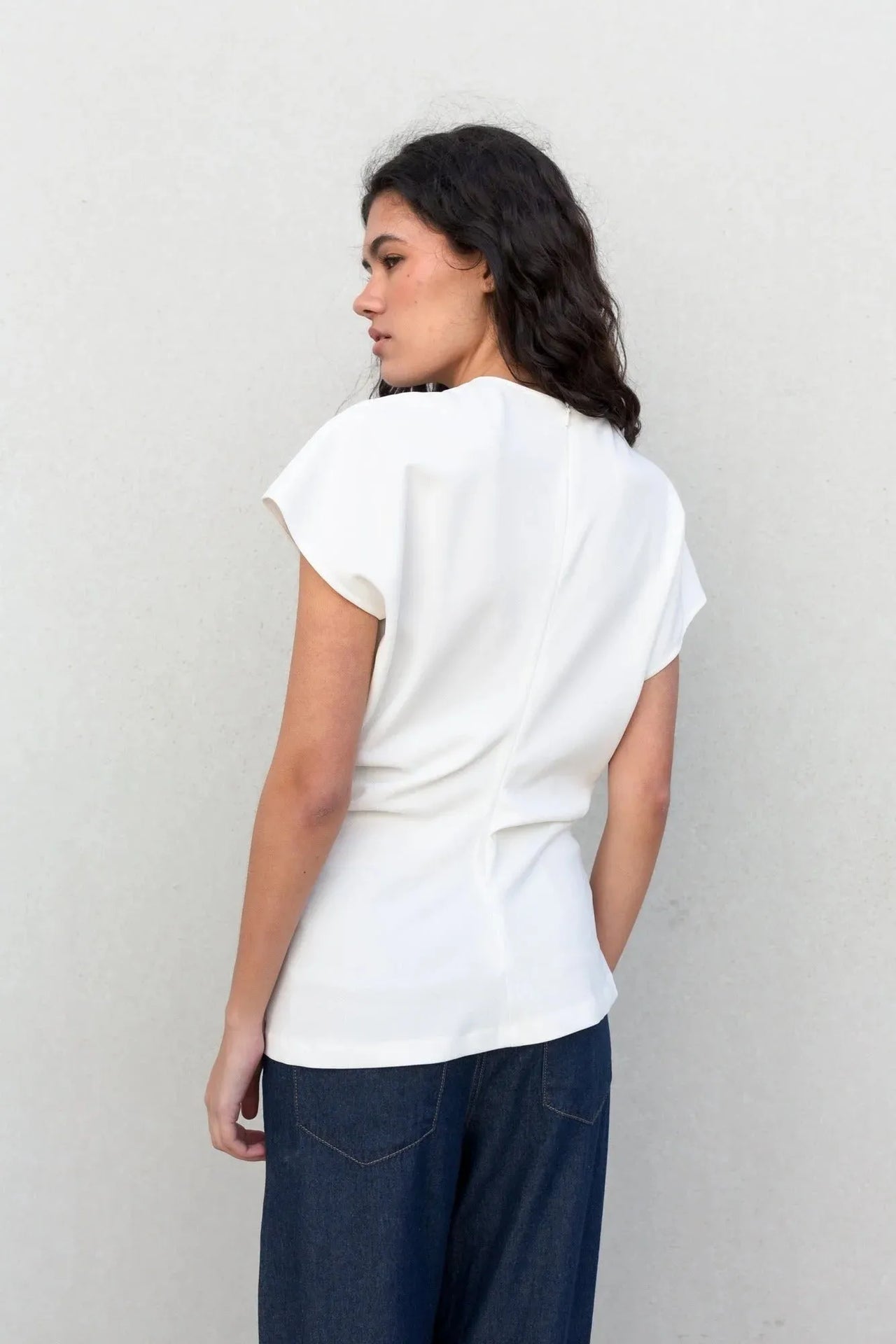 Femme de dos en blouse blanche élégante, montrant le design moderne au niveau du dos, idéal pour un look tendance. Cette blouse blanche femme est un must-have.
