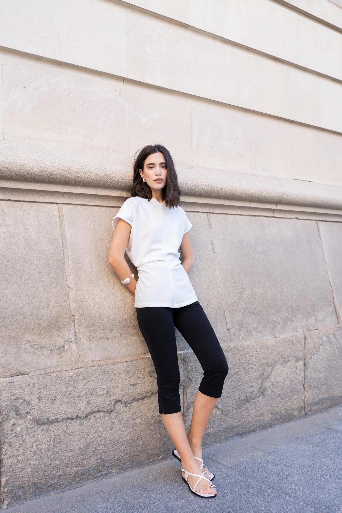 Femme portant une blouse blanche élégante col V minimaliste, t-shirt blanc et sandales blanches