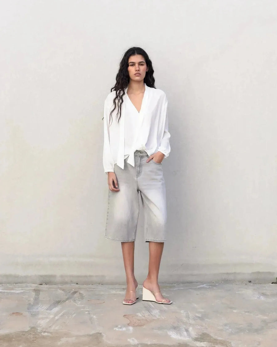 Femme portant une blouse fluide élégante blanche à nouer avec culottes en denim gris