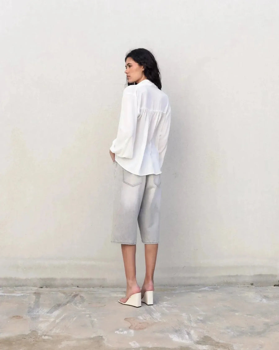 Femme portant une blouse fluide élégante blanche à nouer avec shorts gris et sandales à talons