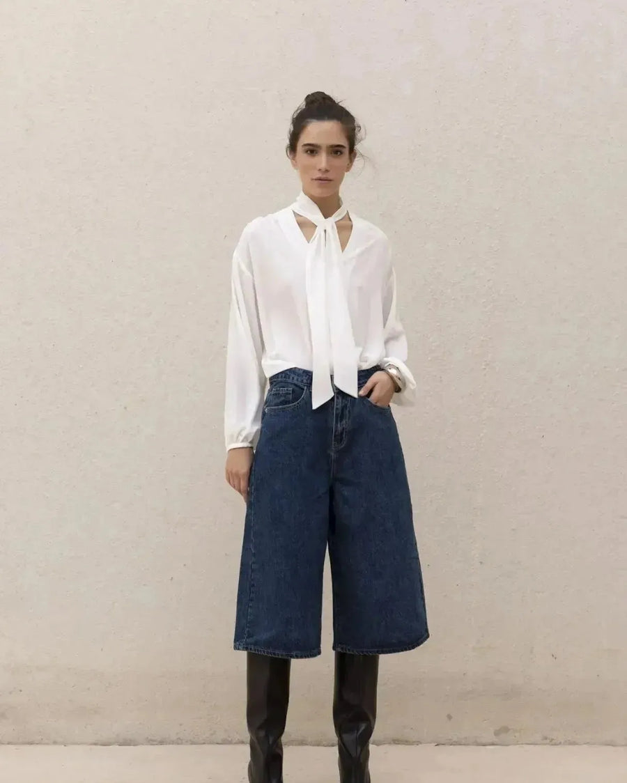 Femme portant une blouse fluide élégante blanche à nouer, culottes en denim et bottes noires