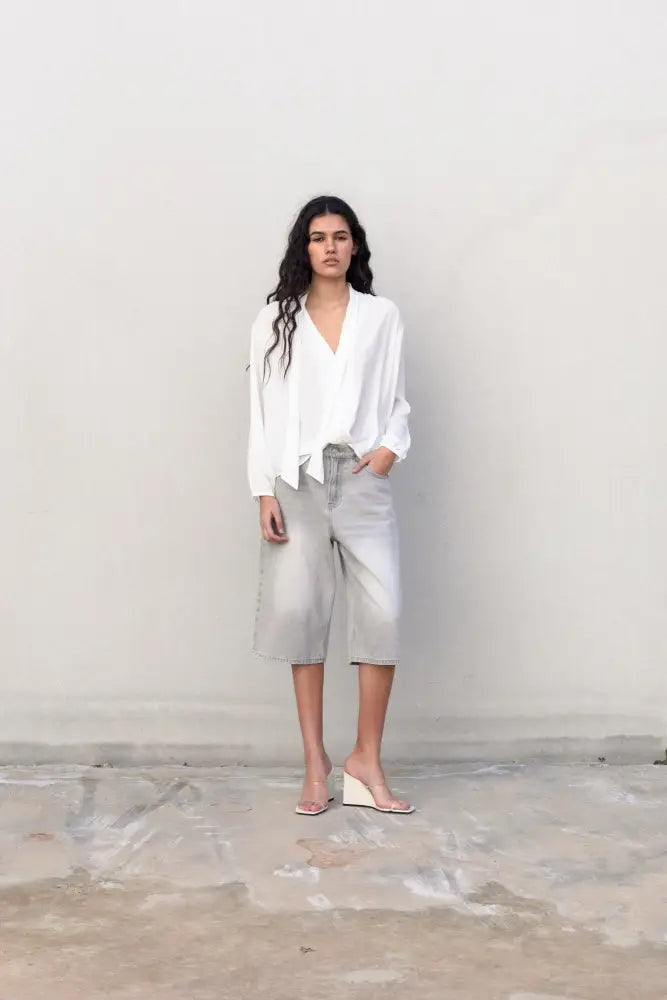 Femme portant une blouse fluide élégante blanche à nouer avec culottes en denim gris