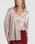 Blouse satinée élégante pour femme avec coupe ample et col chemise, portée par un modèle au teint frais, associée à une jupe rouge.