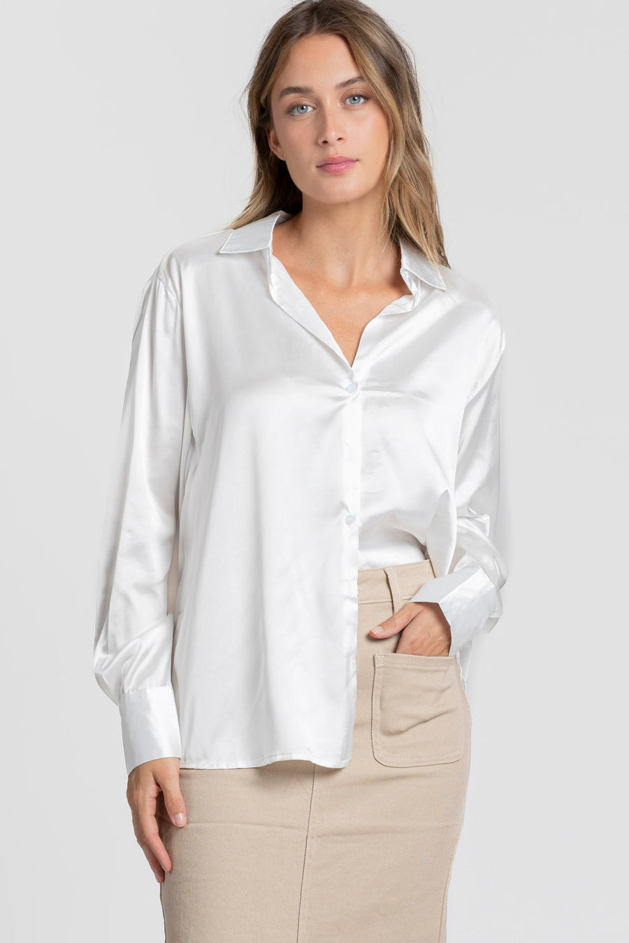 Vue de face d'une blouse satinée femme élégante en blanc, avec col chemise, portée par un modèle avec une jupe beige.