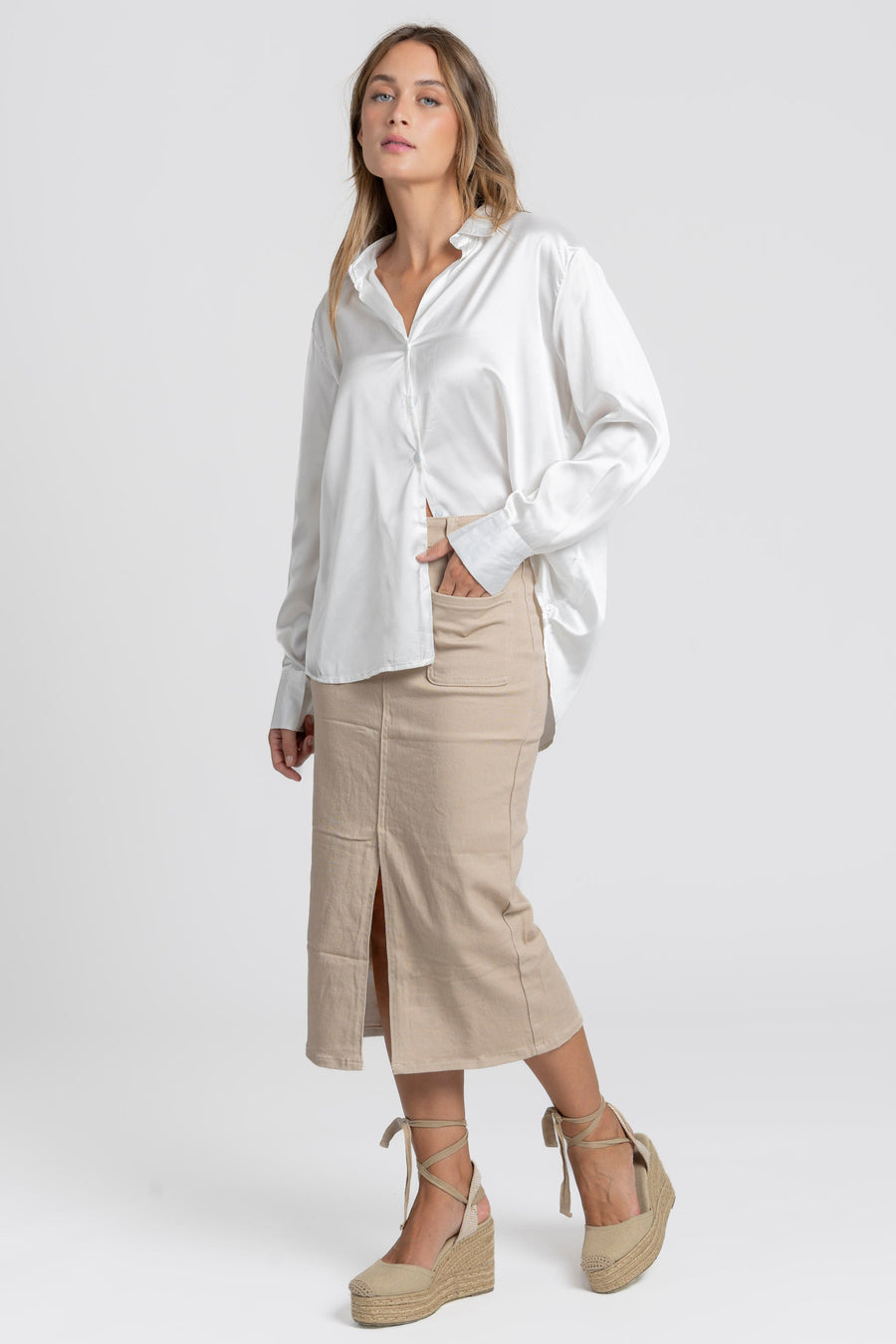 Modèle décontracté en blouse satinée femme élégante blanche, associée à une jupe beige, affichant une silhouette moderne.