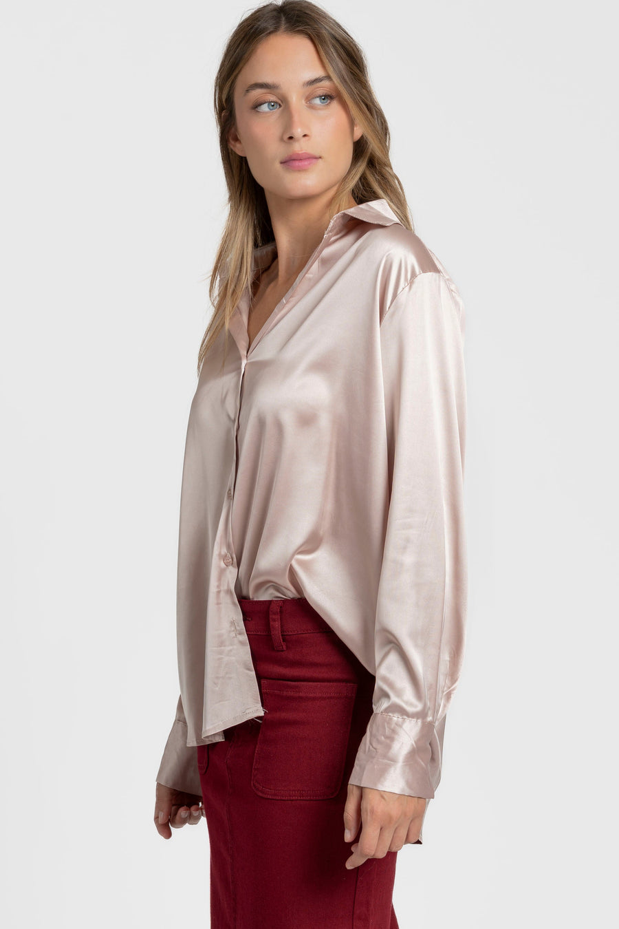 Vue latérale d'une blouse satinée femme élégante, à col chemise, porté par un modèle qui affiche un style chic avec une jupe rouge.