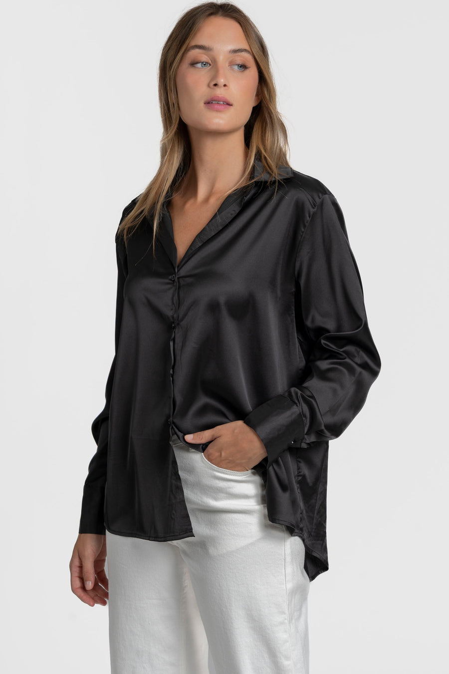 Modèle en blouse satinée femme élégante, en noir, avec une coupe ample et col chemise, accompagnée de pantalons blancs.