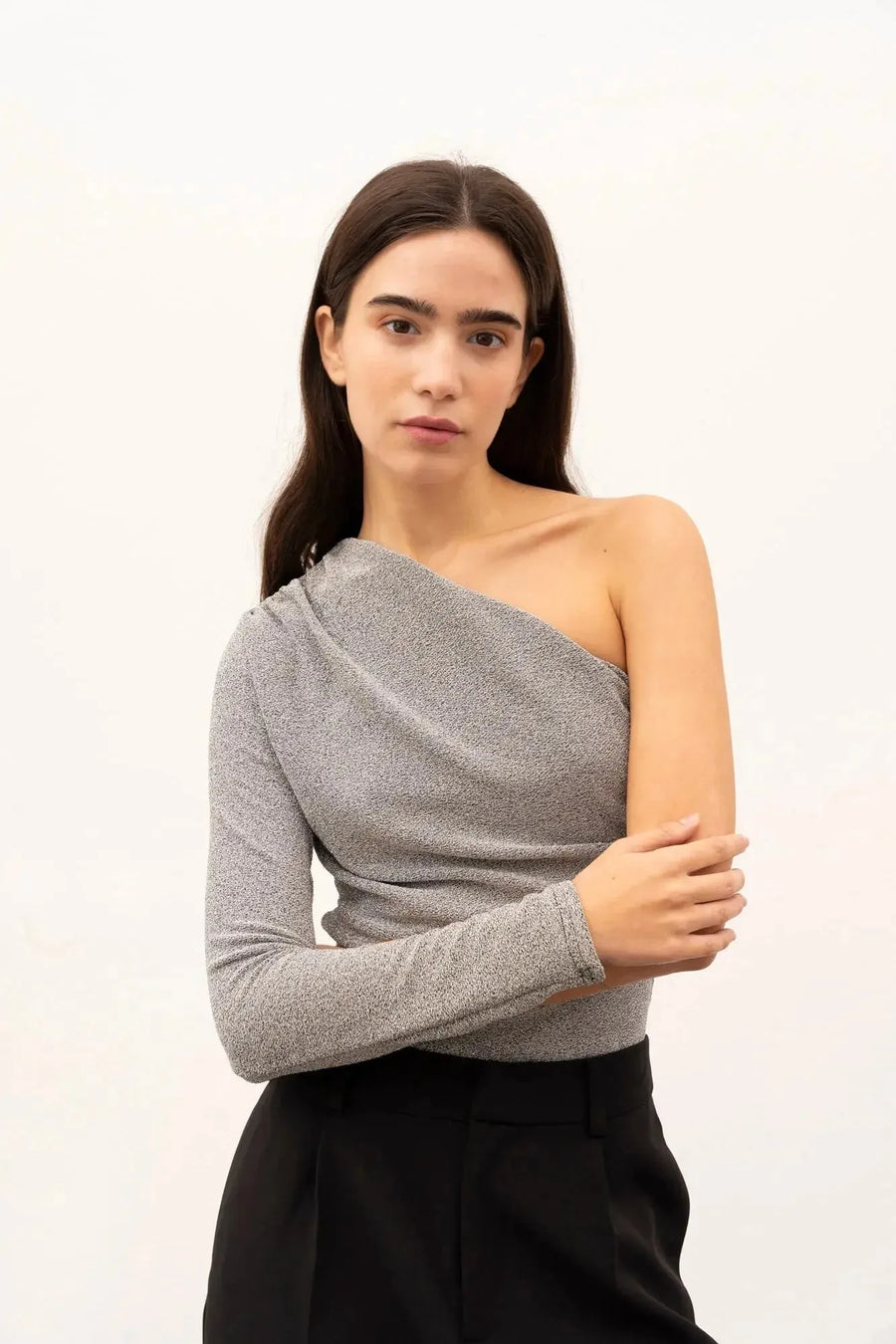 Femme posant avec un body asymétrique, tirant sur les manches pour un effet élégant, parfaite pour un événement spécial.
