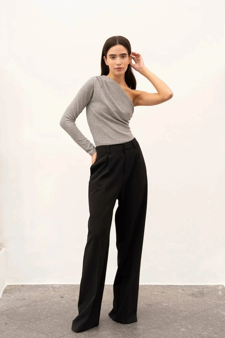 Femme mettant en avant son body asymétrique, combiné avec un pantalon noir, pour un look chic et moderne.