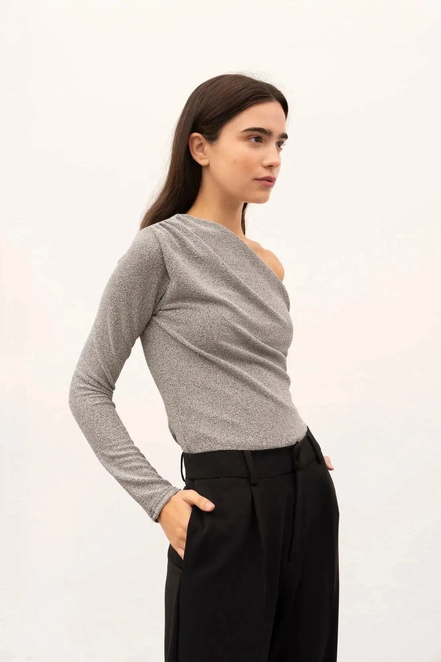 Profil d'une femme portant un body asymétrique, montrant sa coupe unique et sa polyvalence avec un pantalon noir.