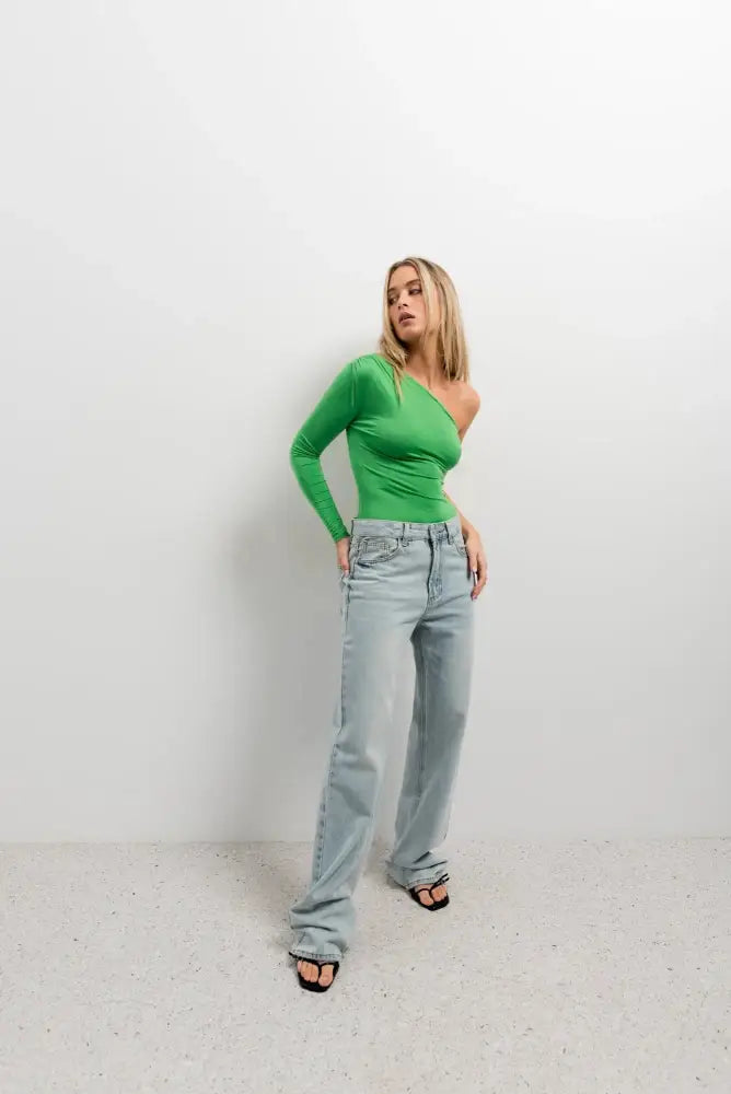 Femme portant un body asymétrique vert à manches longues et jeans larges