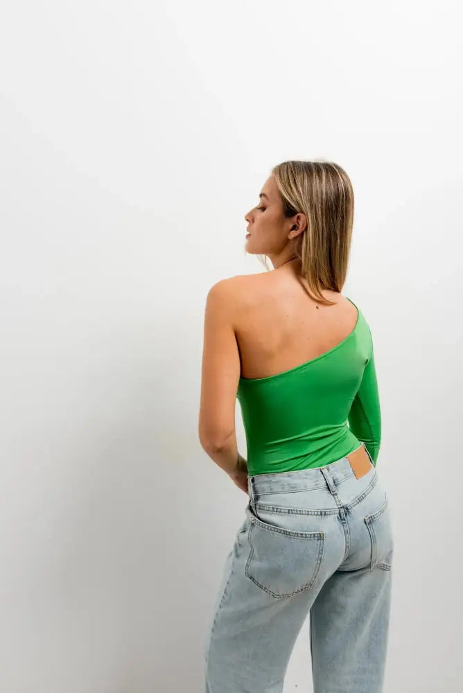 Femme portant un body asymétrique vert à manches longues et jeans délavés clairs