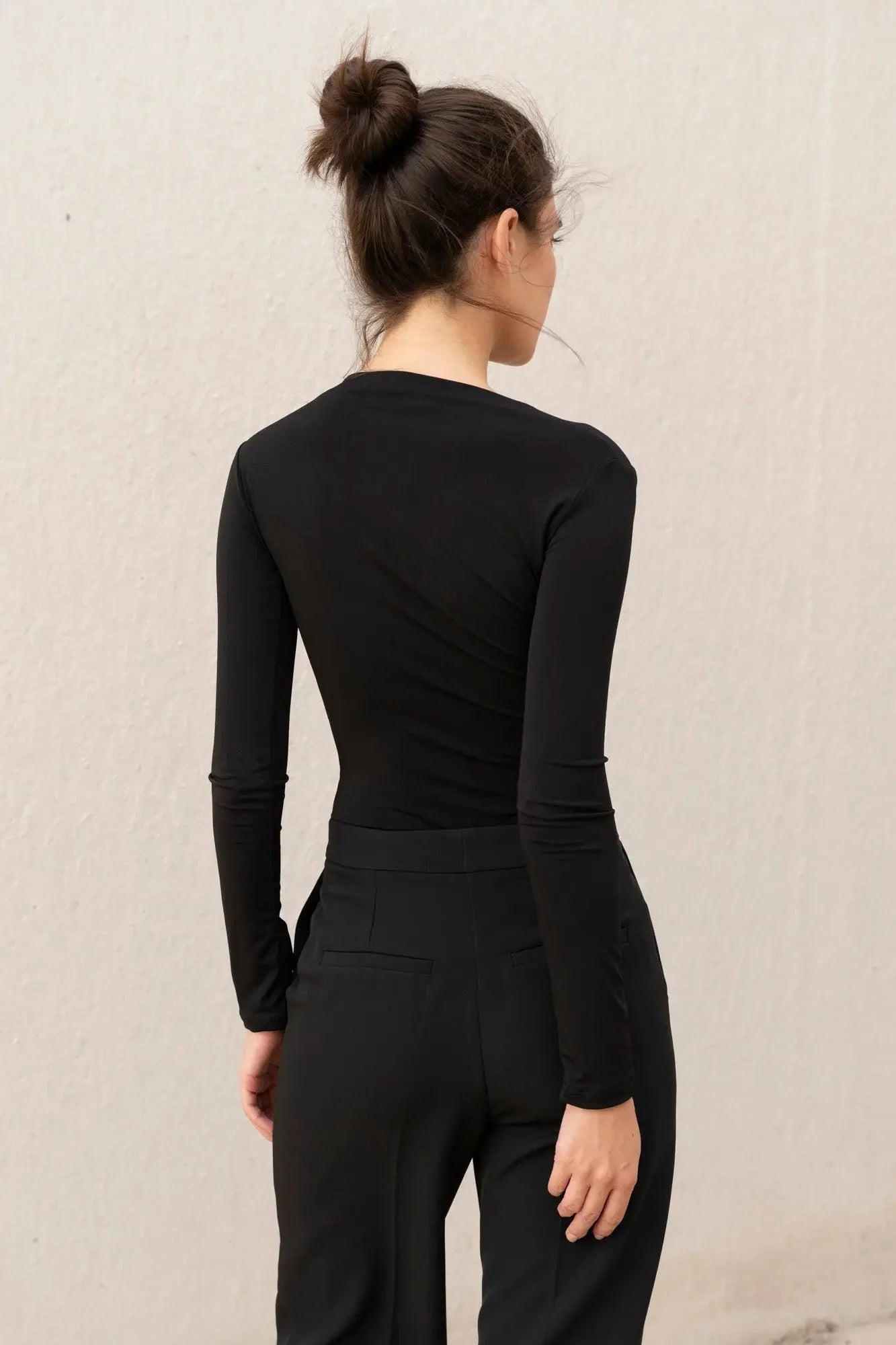 Femme portant le body drapé noir asymétrique en top noir et pantalons noirs