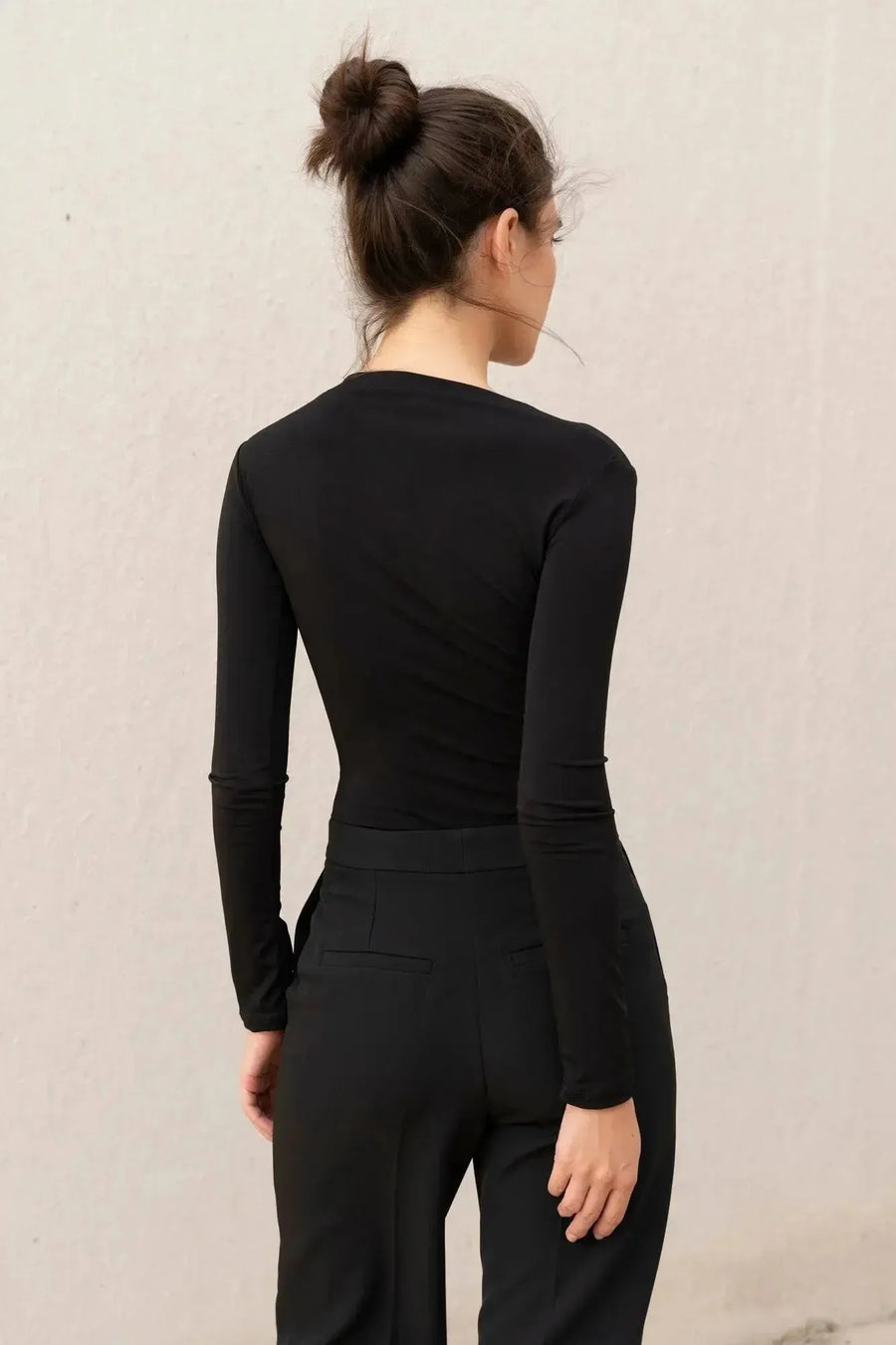 Détail du dos d'un body manche longue femme chic noir drapé asymétrique, soulignant son design moderne et fluide.