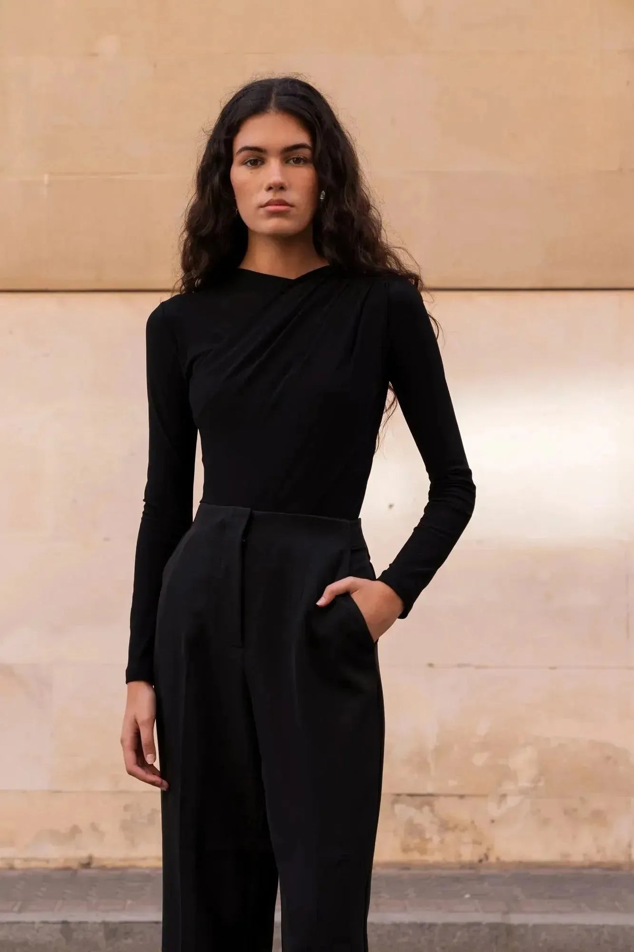 Femme en position calme avec un body manche longue femme chic noir drapé asymétrique, prenant une pose naturelle.