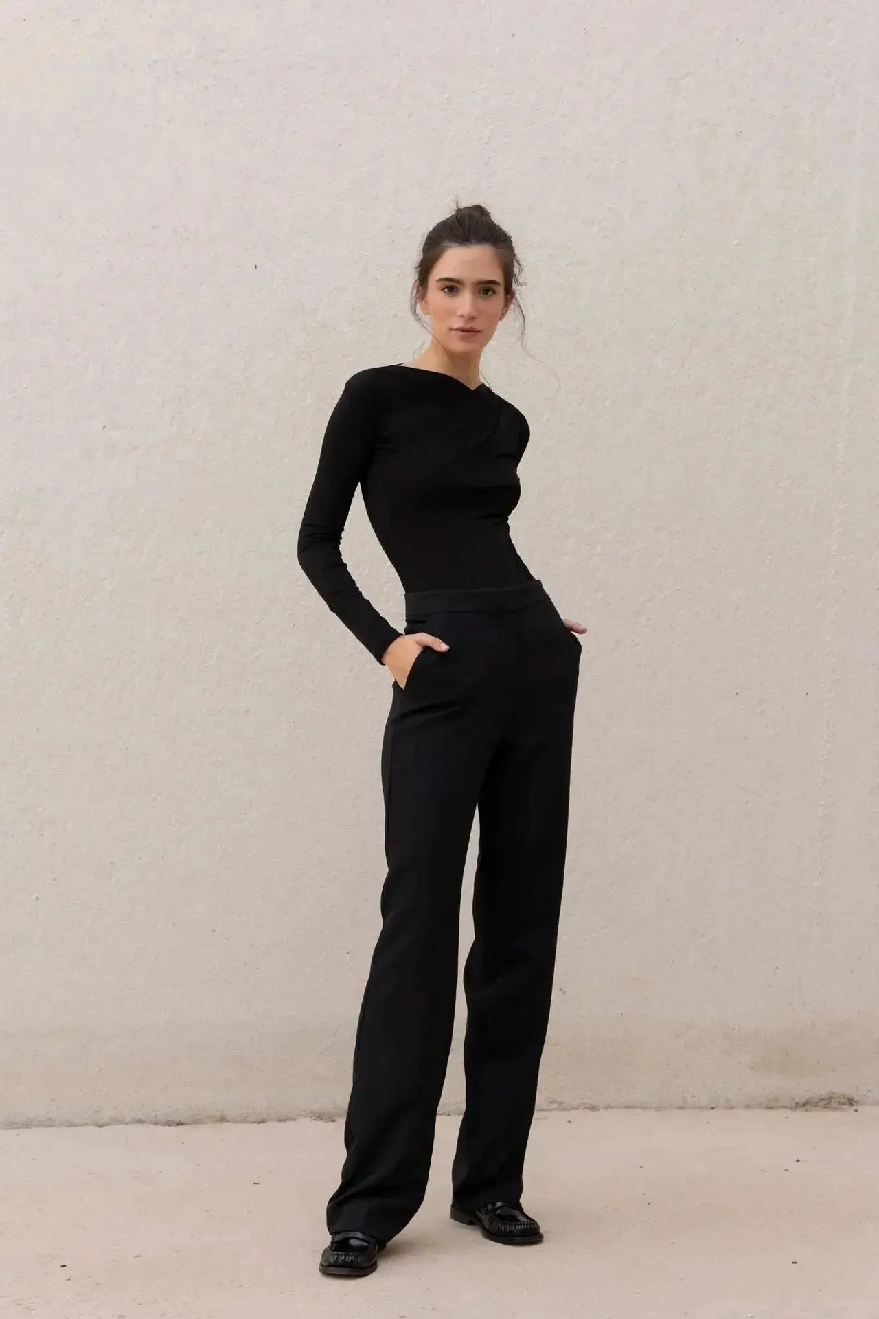 Une femme portant un body manche longue femme chic noir drapé asymétrique, associé à un pantalon noir moderne, illustrant l'élégance et la modernité.