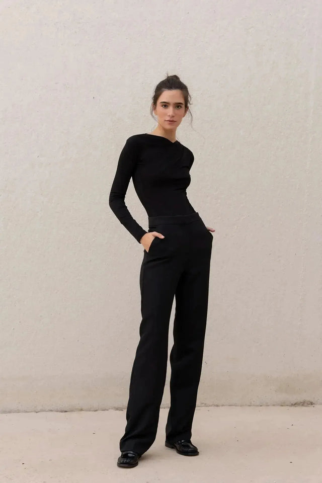Une femme portant un body manche longue femme chic noir drapé asymétrique, associé à un pantalon noir moderne, illustrant l'élégance et la modernité.