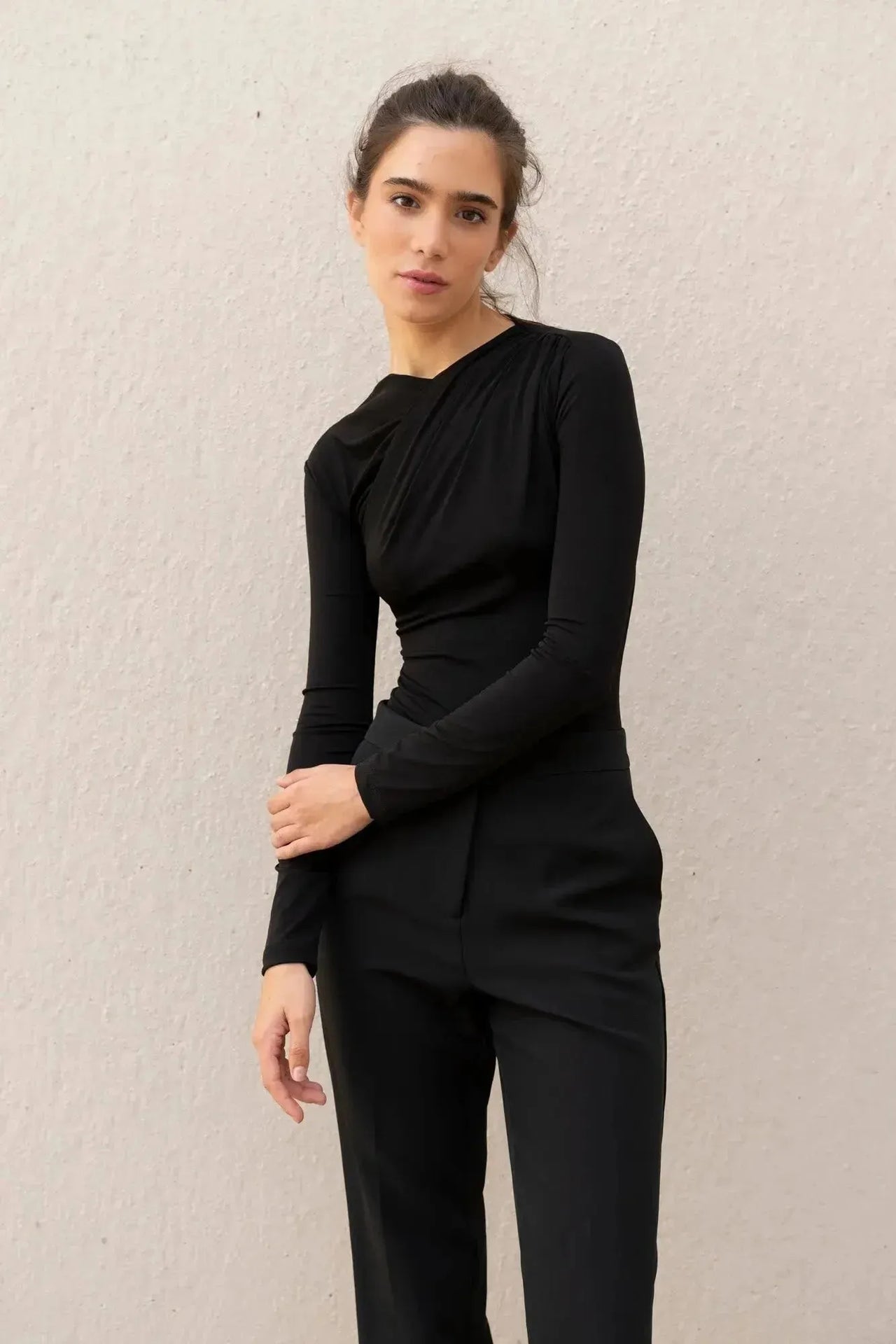 Une femme posant avec confiance dans un body manche longue femme chic noir drapé asymétrique, accentuant son style intemporel.