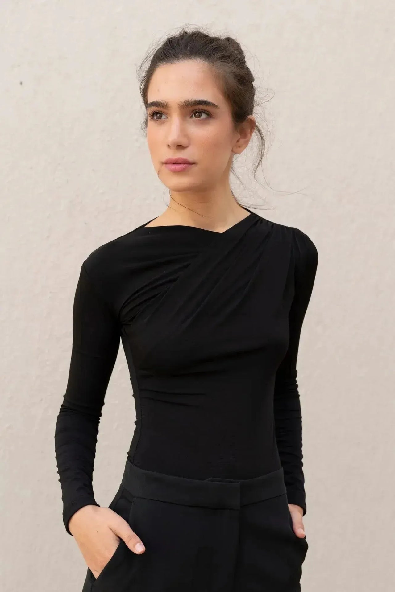 Femme souriante portant un body manche longue femme chic noir drapé asymétrique, montrant une allure sophistiquée.