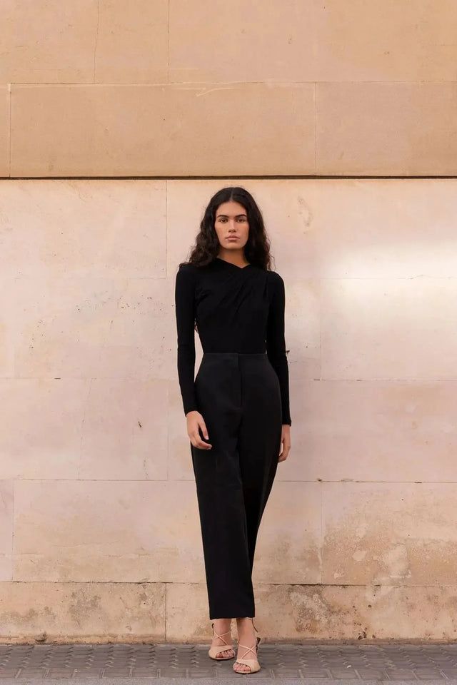 Femme en tenue élégante, portant un body manche longue femme chic noir drapé asymétrique devant un fond architectural.