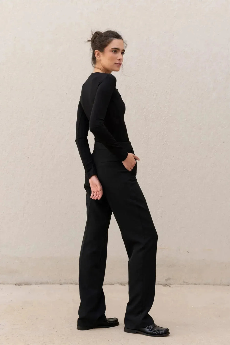Vue de profil d'une femme en body manche longue femme chic noir drapé asymétrique, mettant en valeur sa silhouette élancée.