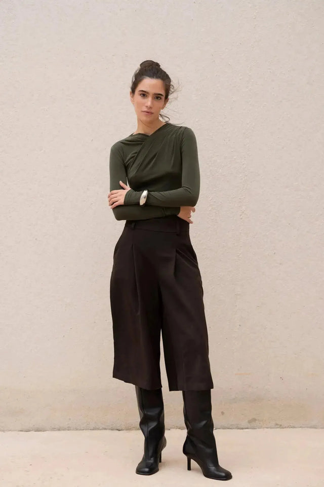 Look chic avec le body vert olive asymétrique et un pantalon noir, mannequin en pose.