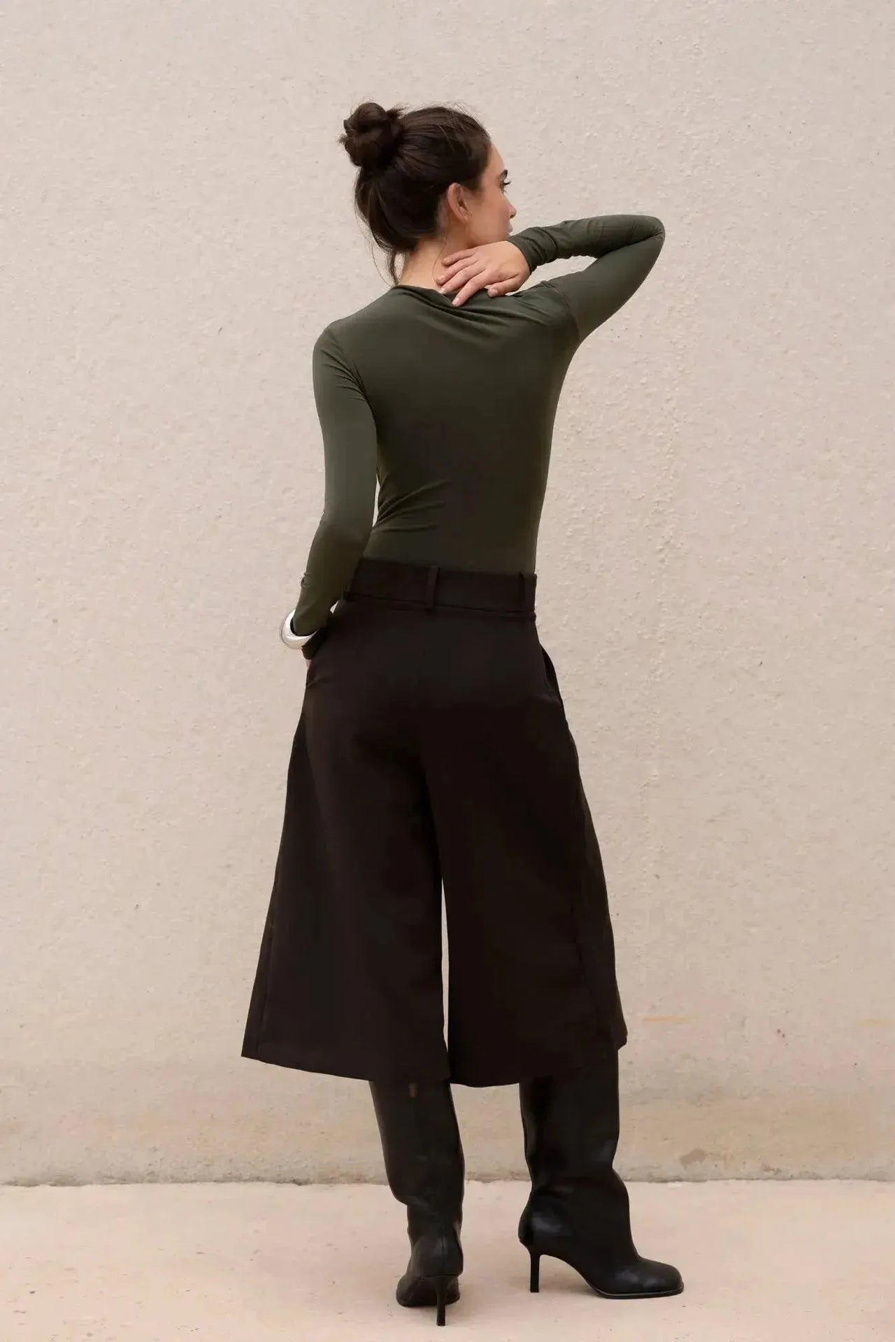 Modèle féminin avec un body vert olive asymétrique et pantalon noir, vue arrière.