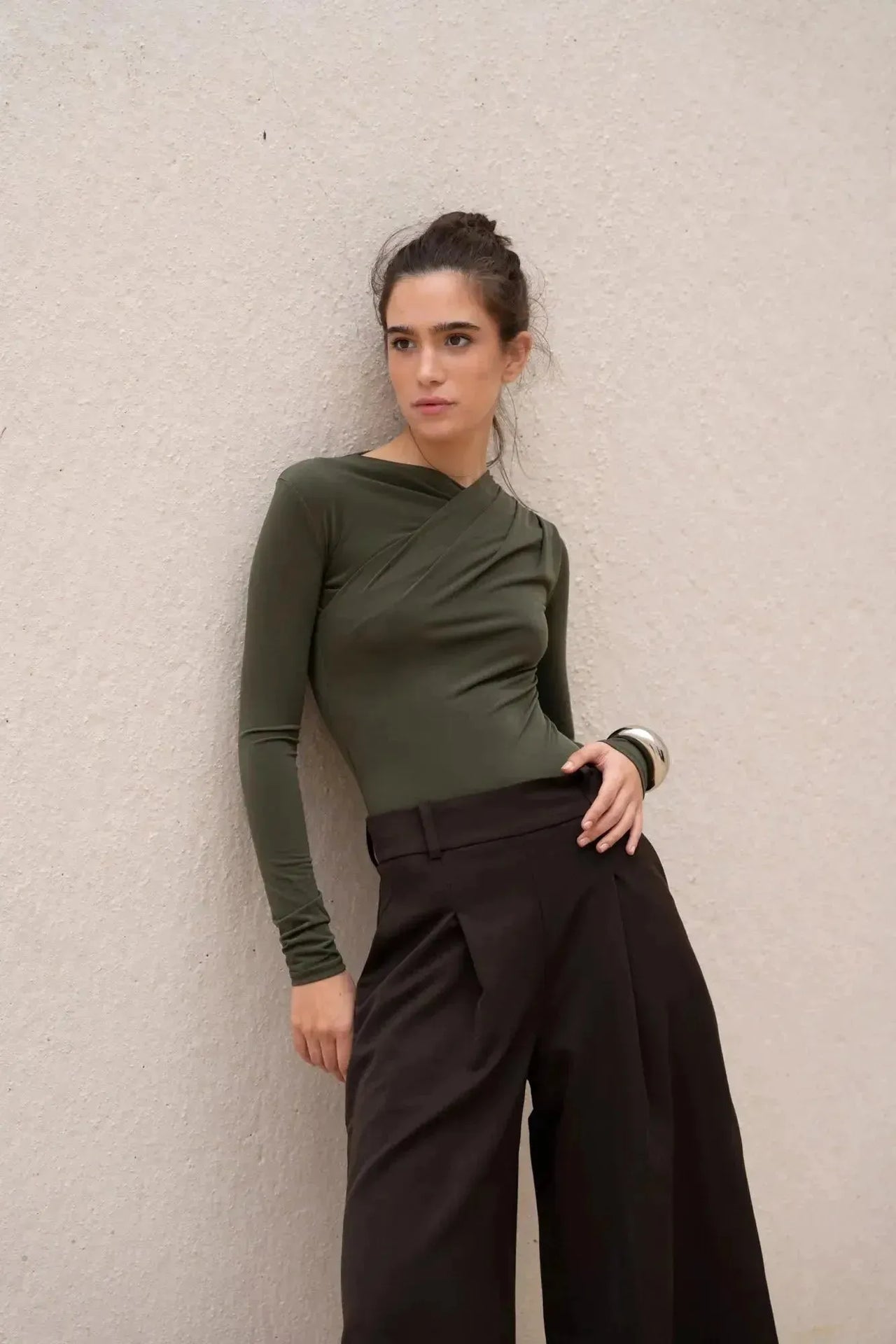 Body vert olive asymétrique avec drapé élégant, manches longues, porté par un modèle avec un pantalon large.