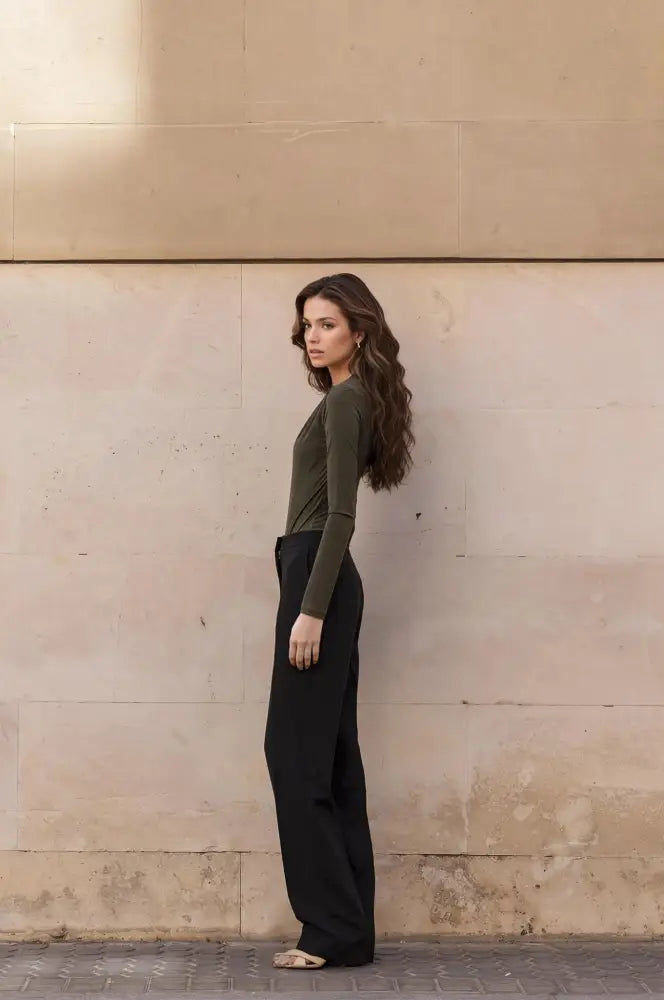 Femme portant un body drapé vert asymétrique avec top vert olive et pantalons noirs