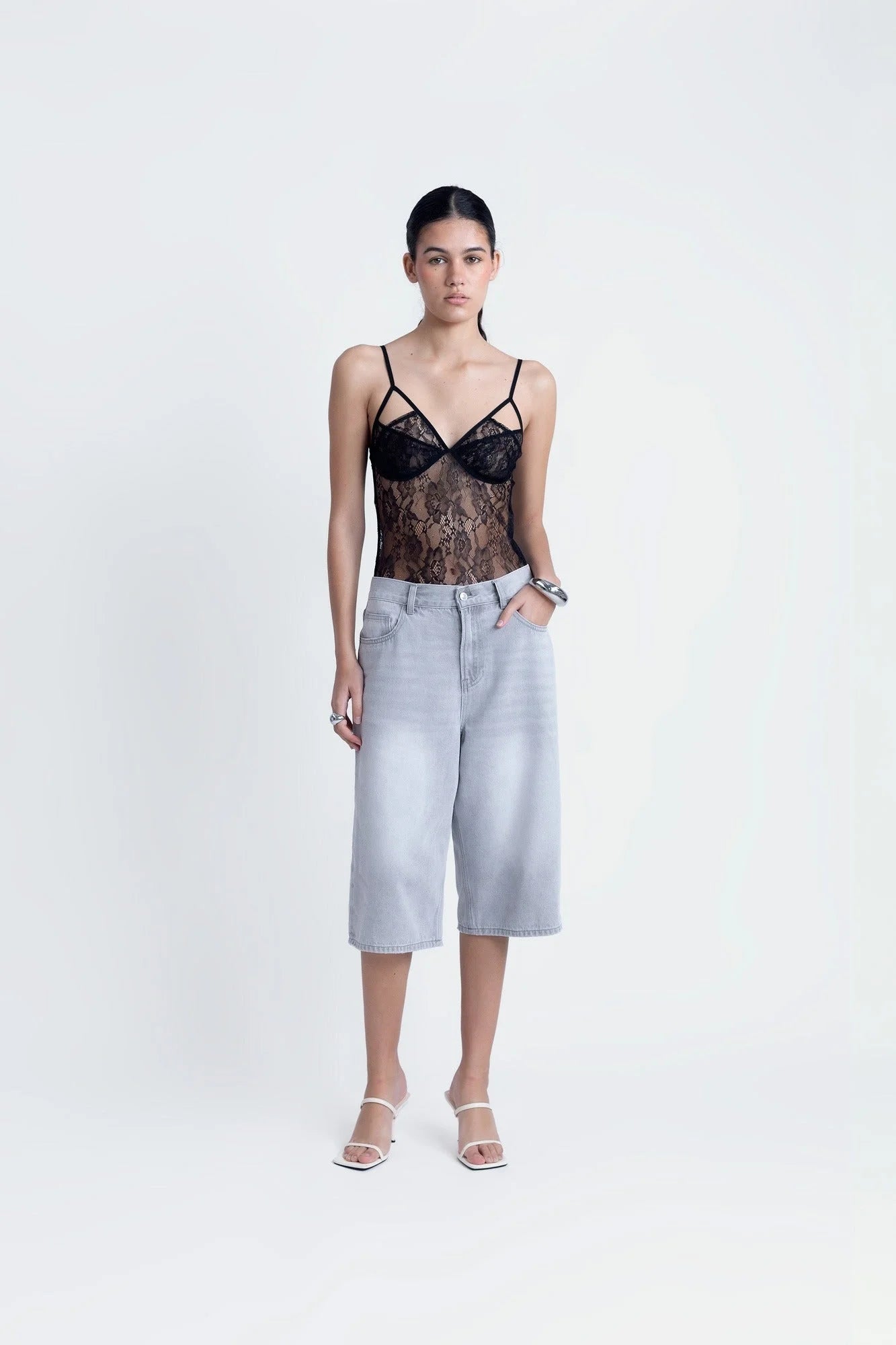 Body en dentelle noire à bretelles fines porté avec culottes en denim clair et talons hauts blancs