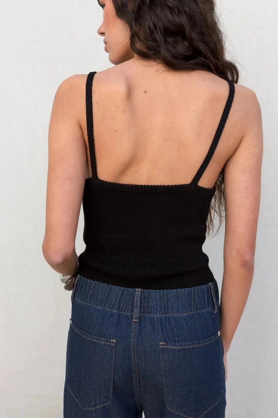 Femme en haut noir montrant le dos tout en portant un jean élastique femme, pantalon fluide effet denim noir.