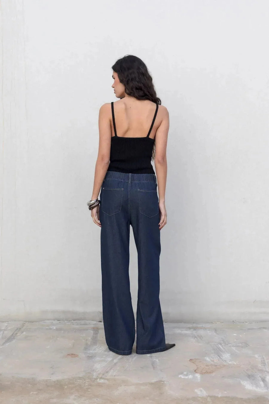 Vue arrière d'une femme en jean élastique femme, avec un haut noir, pantalon fluide effet denim noir.