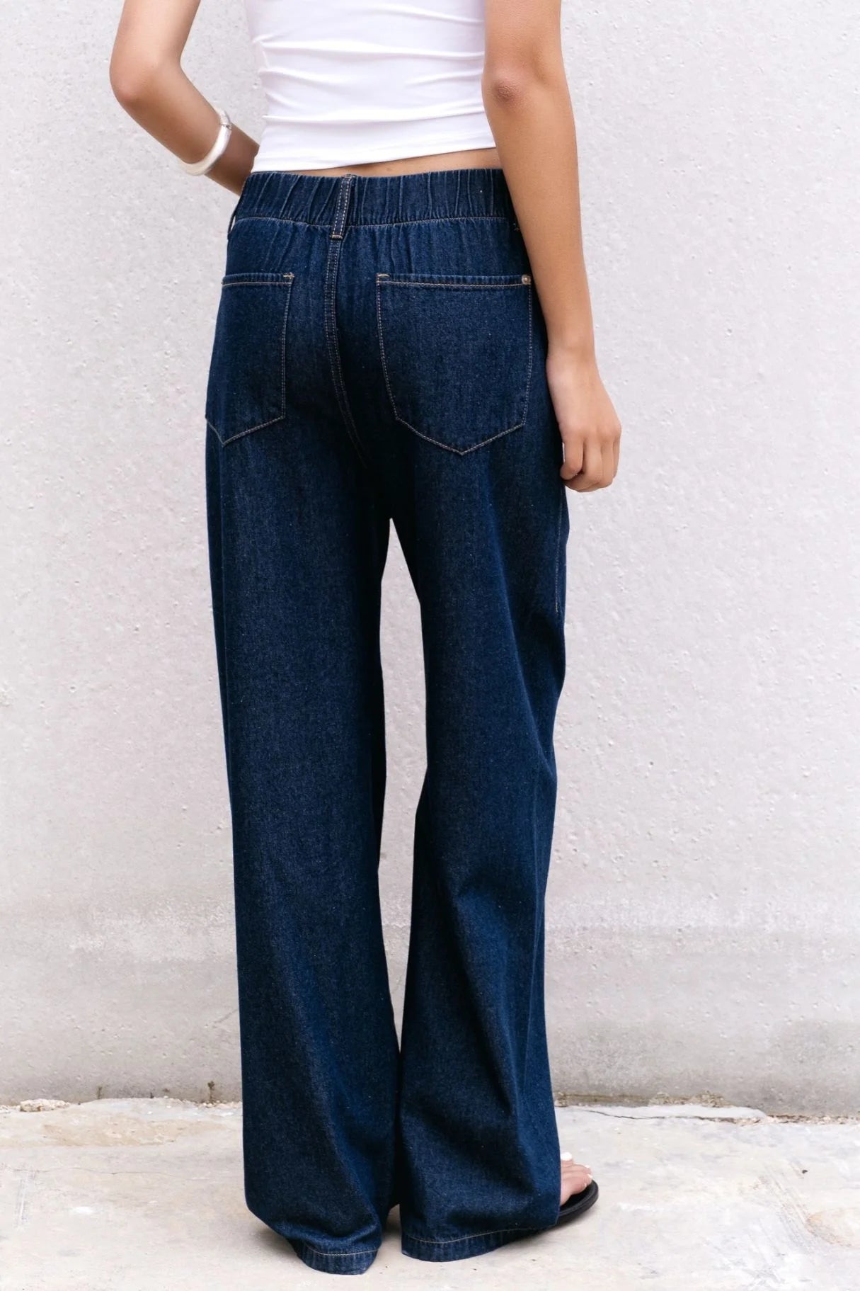 Vue arrière d'une femme dans un jean élastique femme, pantalon fluide effet denim noir, avec un top blanc.