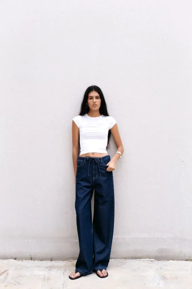 Femme portant un haut court blanc et un pantalon fluide effet denim bleu foncé