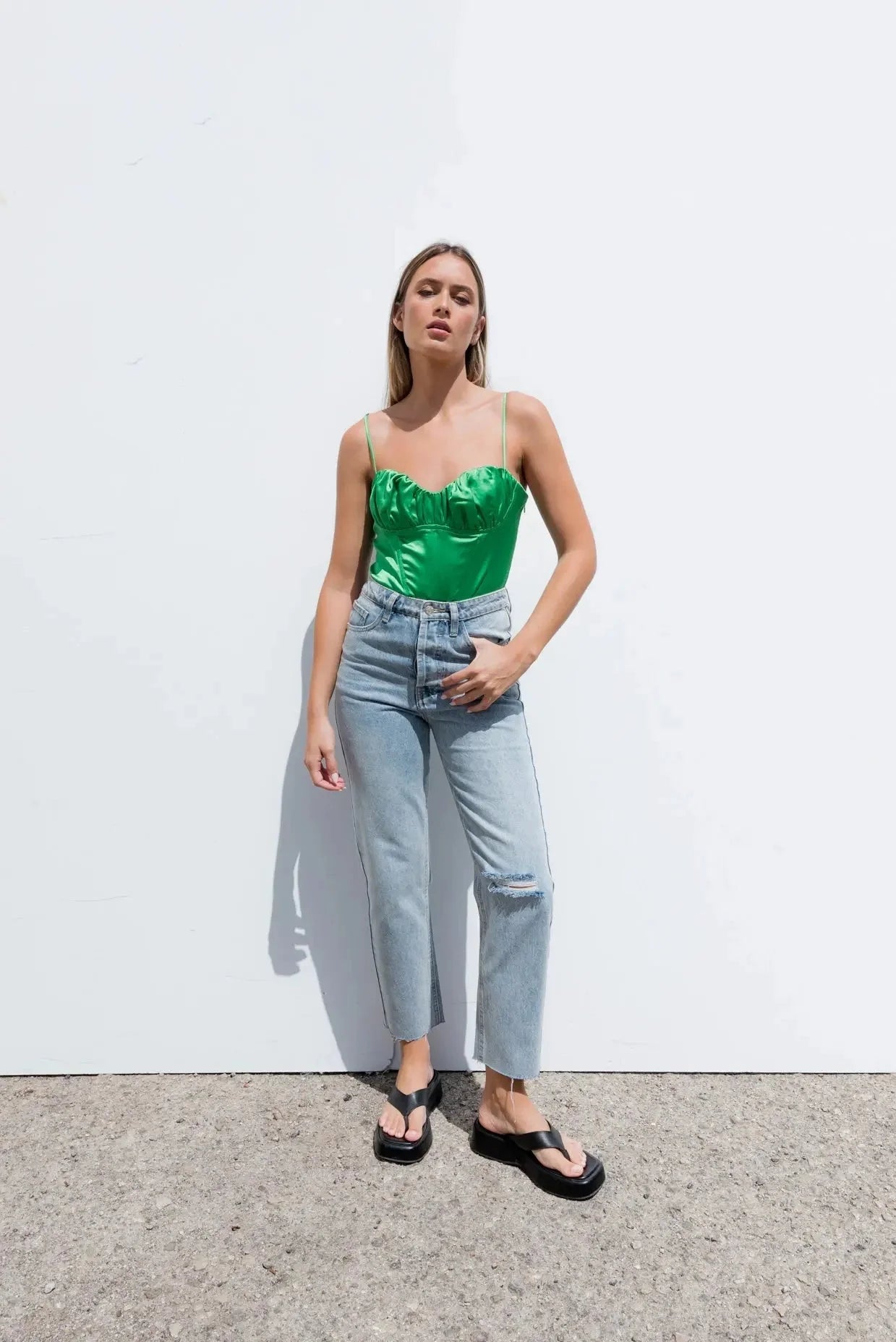 Une femme portant une camisole satin vert effet corset, jeans droits délavés et sandales noires