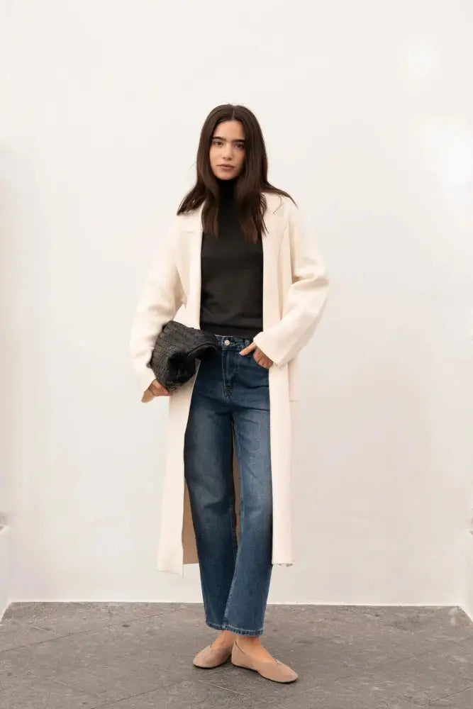 Femme en maille oversize cosy chic avec manteau crème, turtleneck noir et ballerines pâles