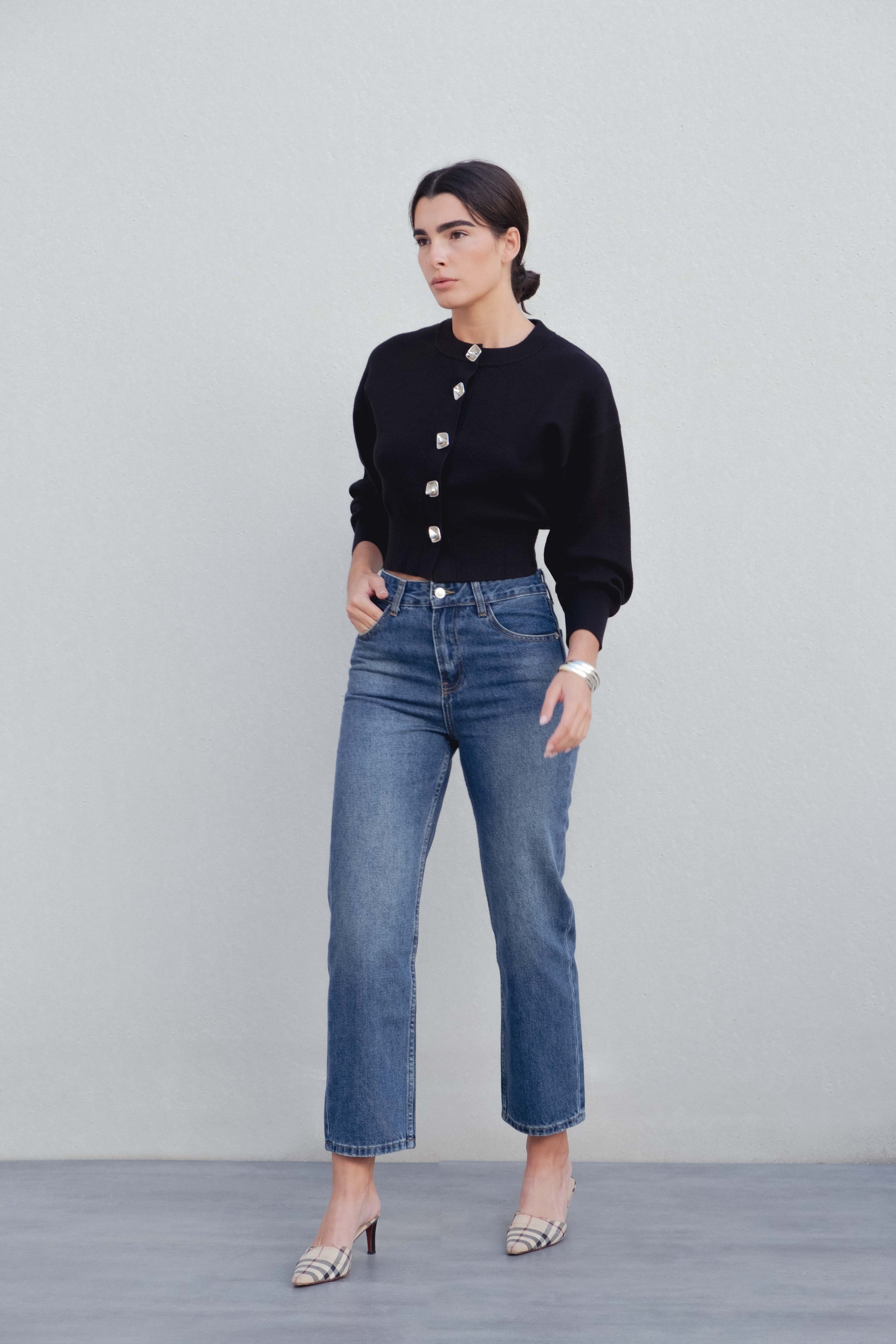 Femme vêtue d'un cardigan noir boutonné cintré, se tenant avec confiance, associé à des jeans. Cardigan noir femme.