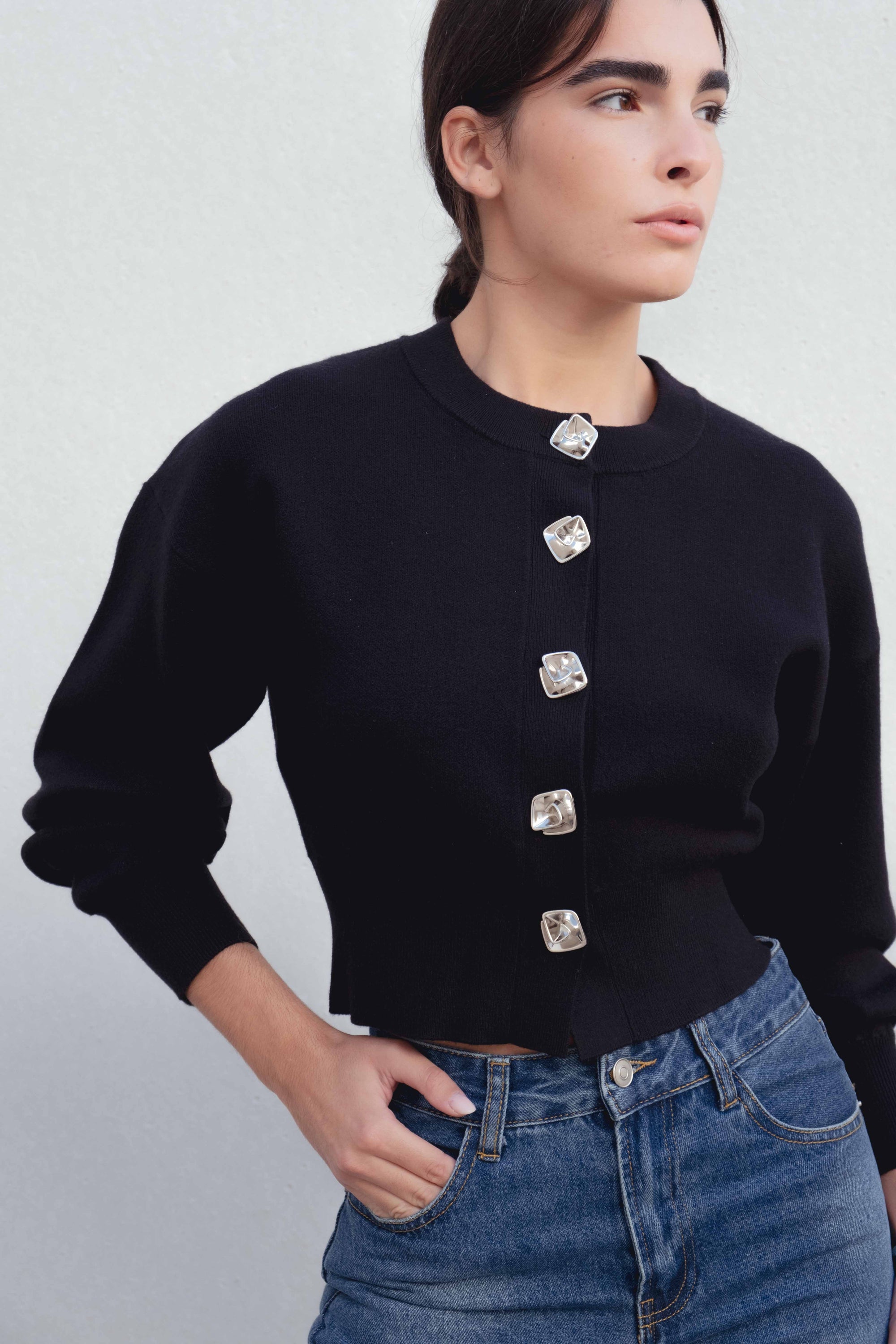 Gros plan sur une femme portant un cardigan noir boutonné cintré, illustrant les détails des boutons et le style chic. Cardigan noir femme.
