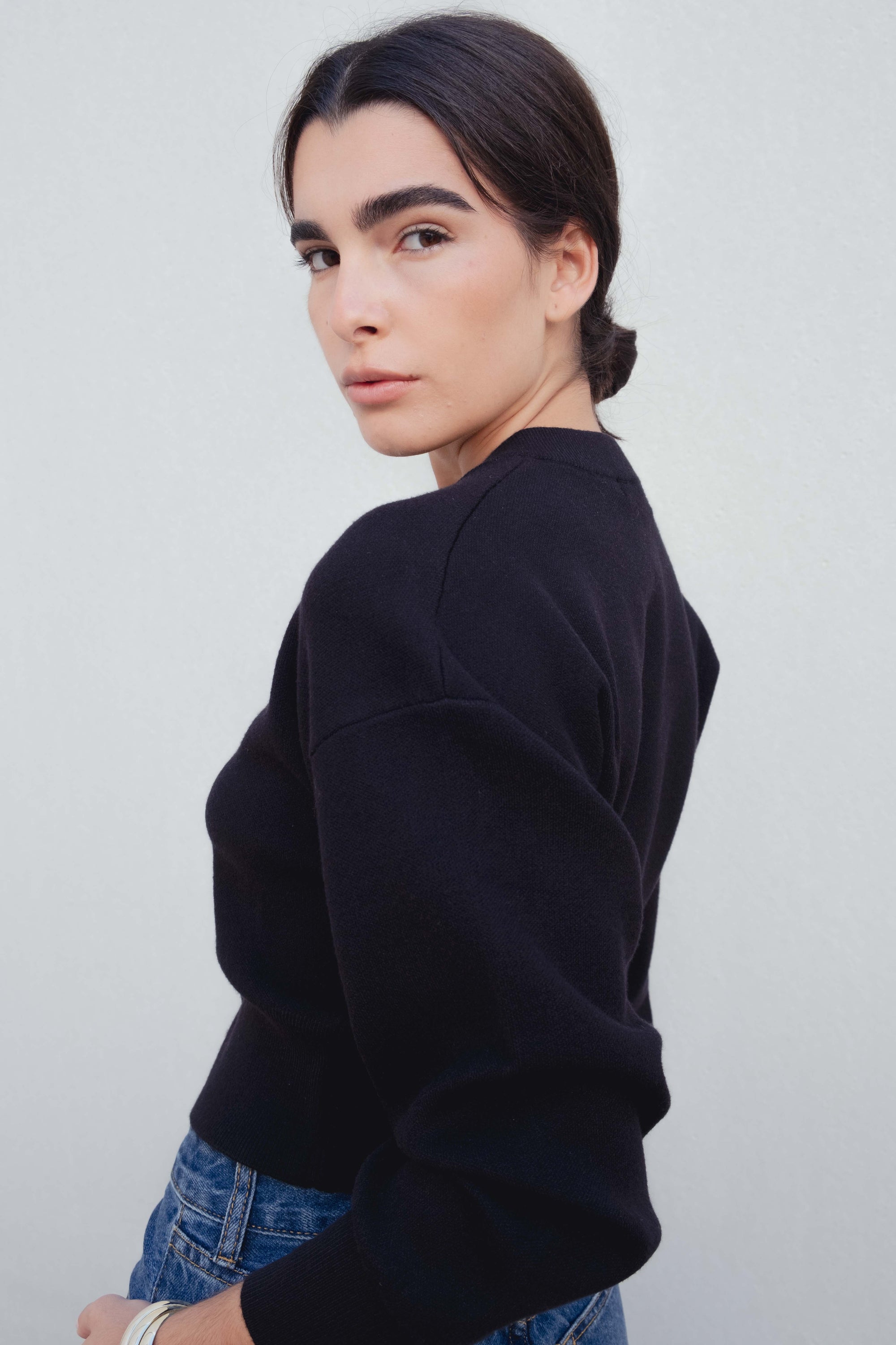 Femme de profil, affichant un cardigan noir boutonné cintré qui souligne sa silhouette, tout en portant des jeans. Cardigan noir femme.