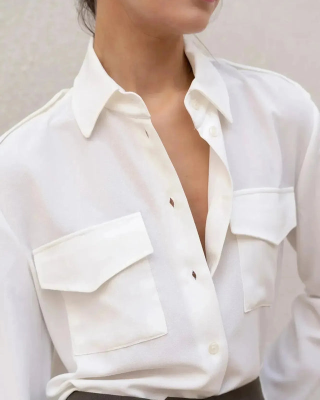 Détail de la chemise blanche en soie à poches pour femme, mettant en valeur les boutons et le tissu léger, idéale pour un style décontracté.