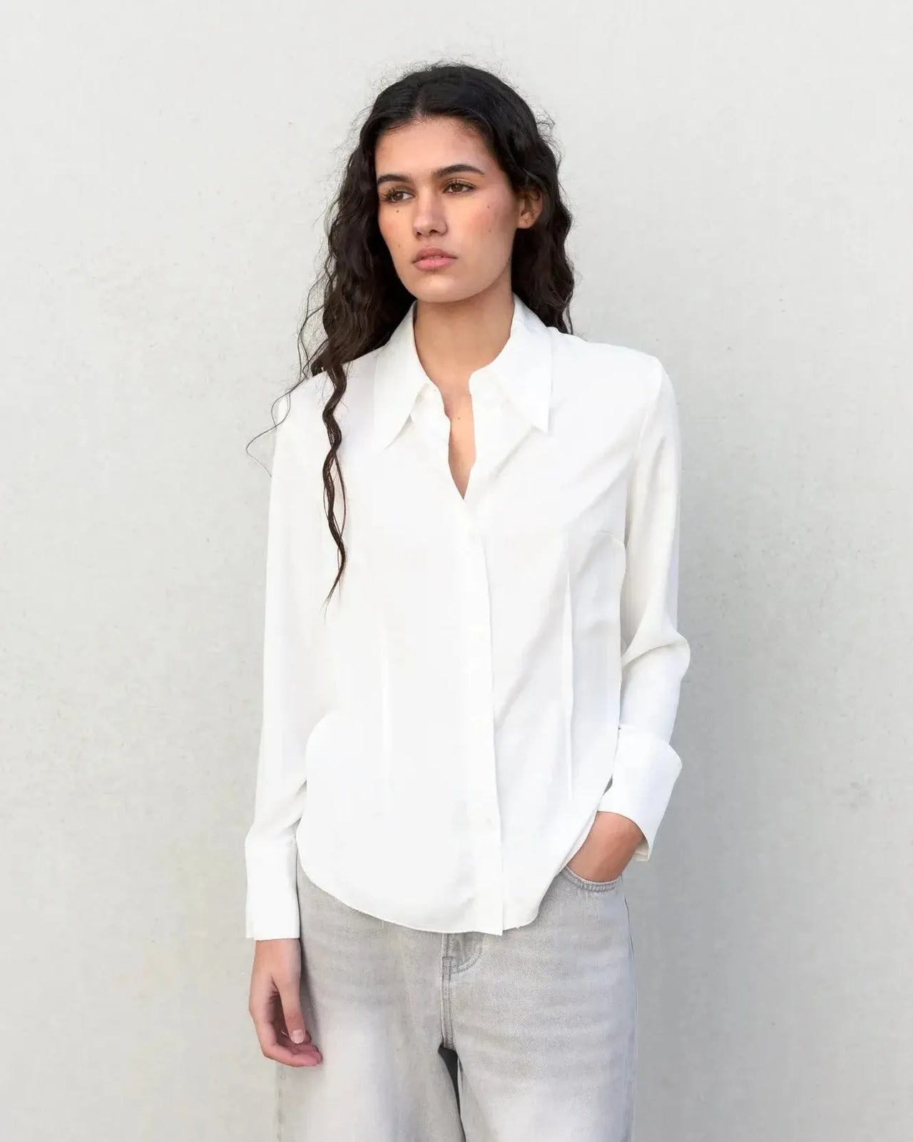 Modèle portant une chemise blanche femme grand col ajustée à pinces, look élégant et professionnel.