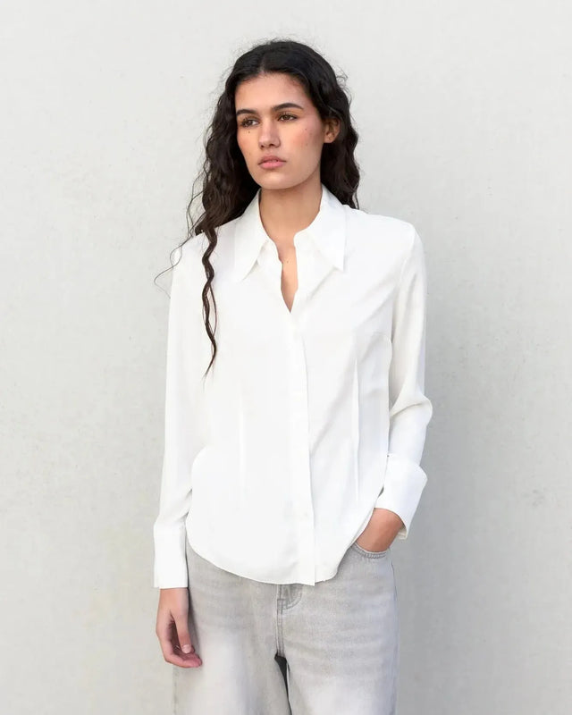 Modèle portant une chemise blanche femme grand col ajustée à pinces, look élégant et professionnel.
