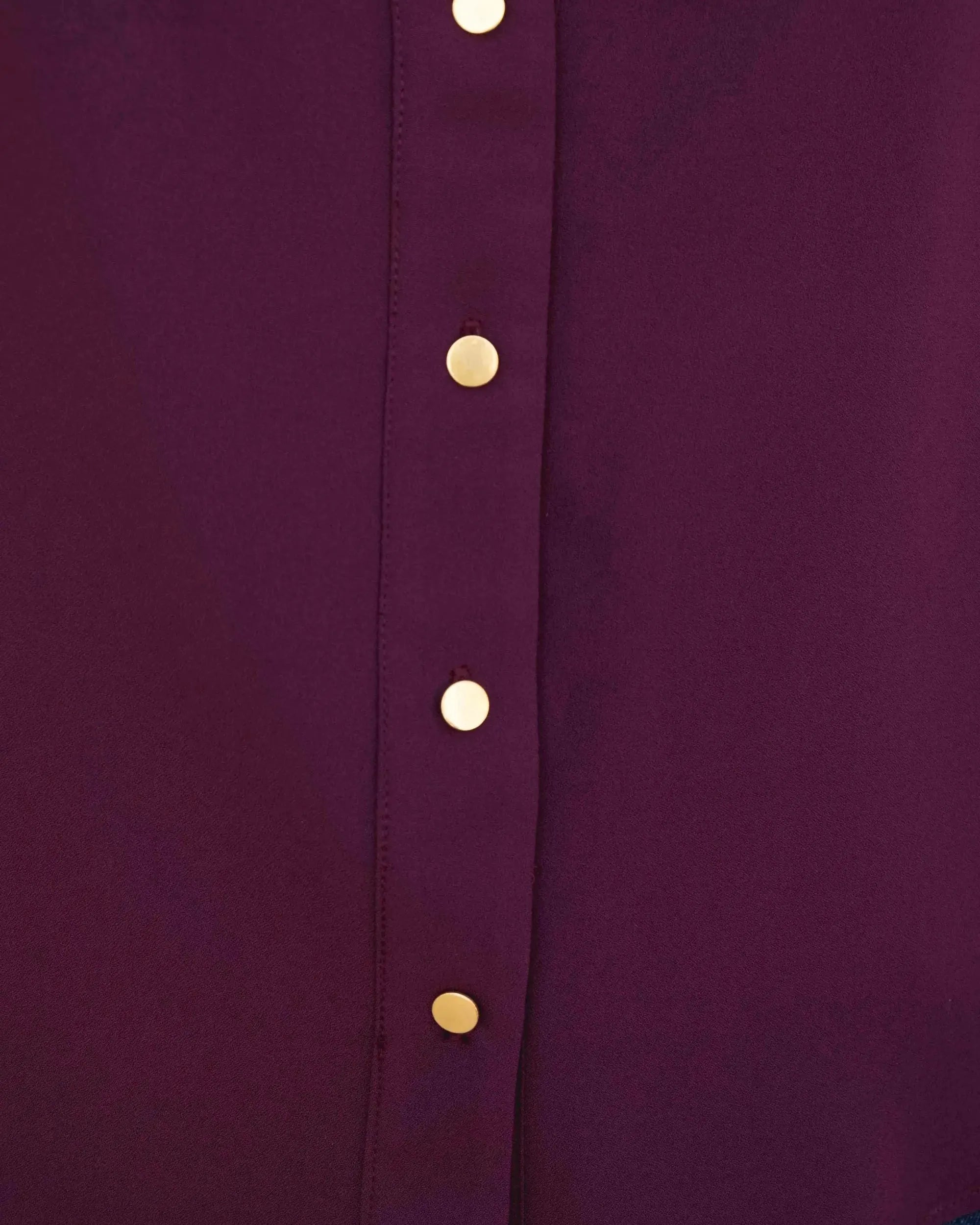Gros plan sur le boutonnage doré de la chemise élégante bordeaux à boutons dorés pour femme, mettant en avant son design chic. Une pièce clé pour le look ultime de chemise bordeaux femme.