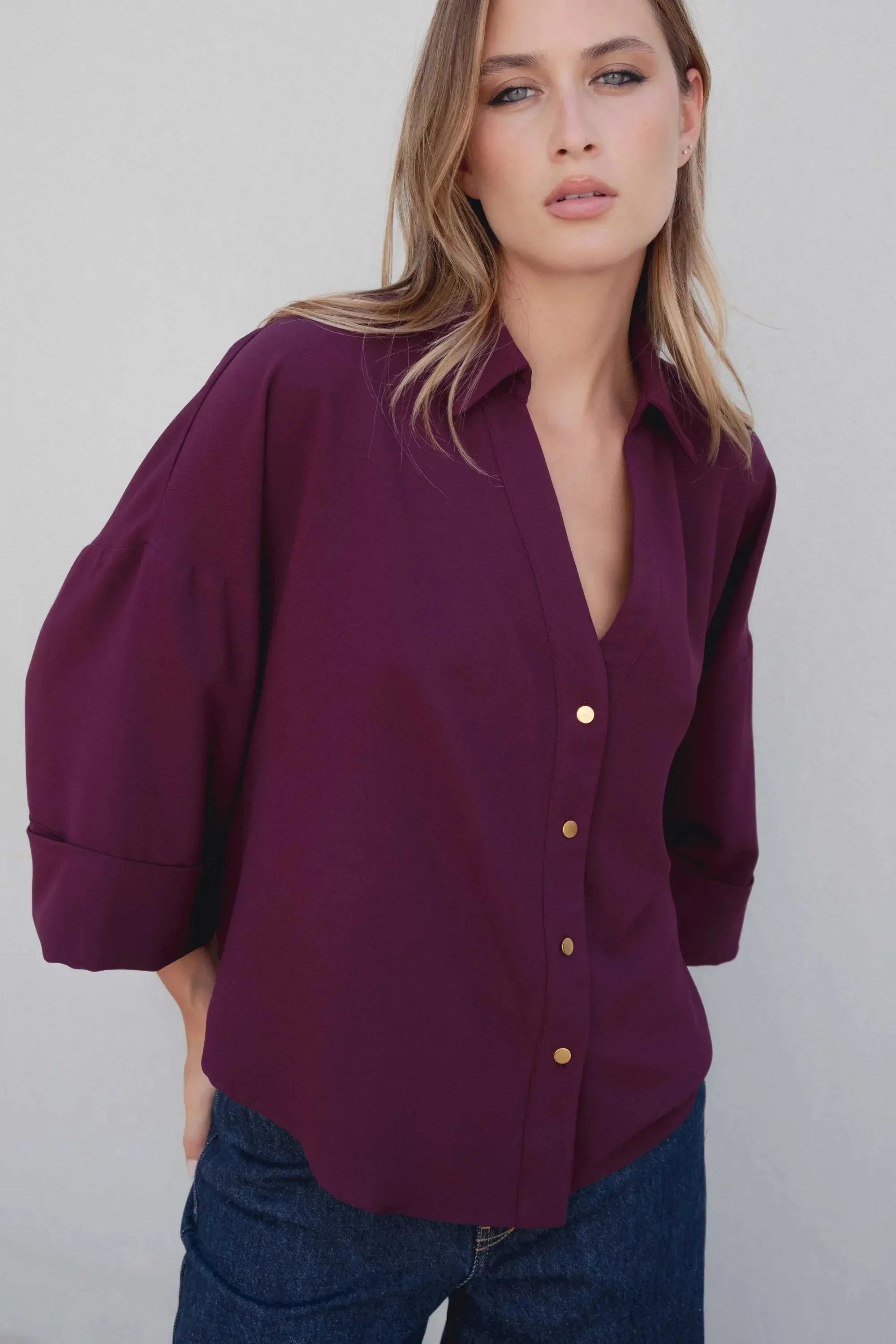Chemise élégante bordeaux à boutons dorés pour femme, style ample avec des manches bouffantes, présentée sur une femme dans un look décontracté. Idéale pour un style chic et moderne, parfaite comme chemise bordeaux femme.