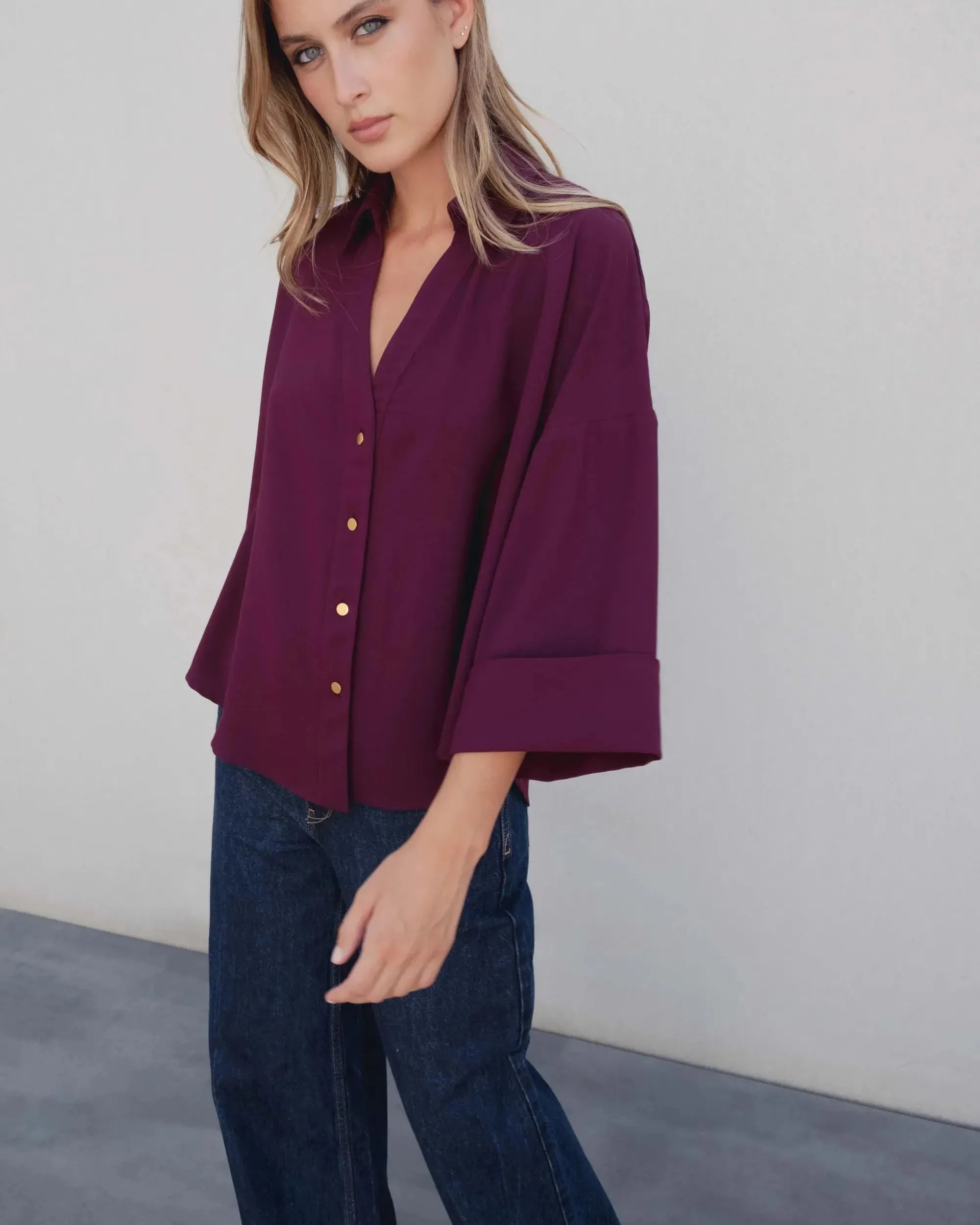 Vue de profil d'une femme portant une chemise élégante bordeaux à boutons dorés, mettant en avant les détails tendance de la coupe ample. Parfaite pour un style élégant en tant que chemise bordeaux femme.